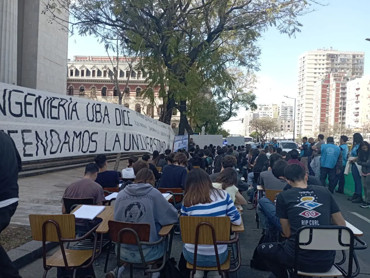 Estudiantes cursando una clase pública en la calle, frente a la facultad